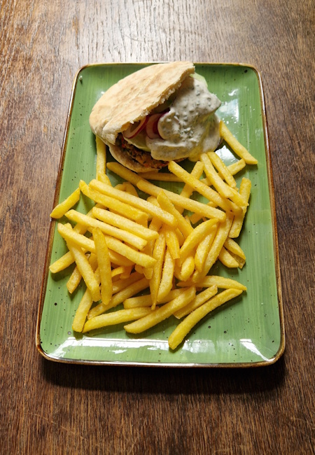 falafel im pitabrot mit tomaten, gurken, zwiebeln und joghurtsoße mit pommes 
                 der teller steht auf einem alten holztisch